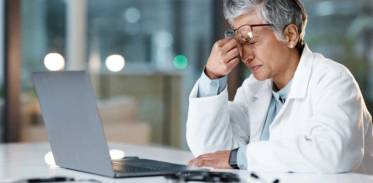 Mediziner sich den Nasenrücken drückend vor dem Computer bei Stress