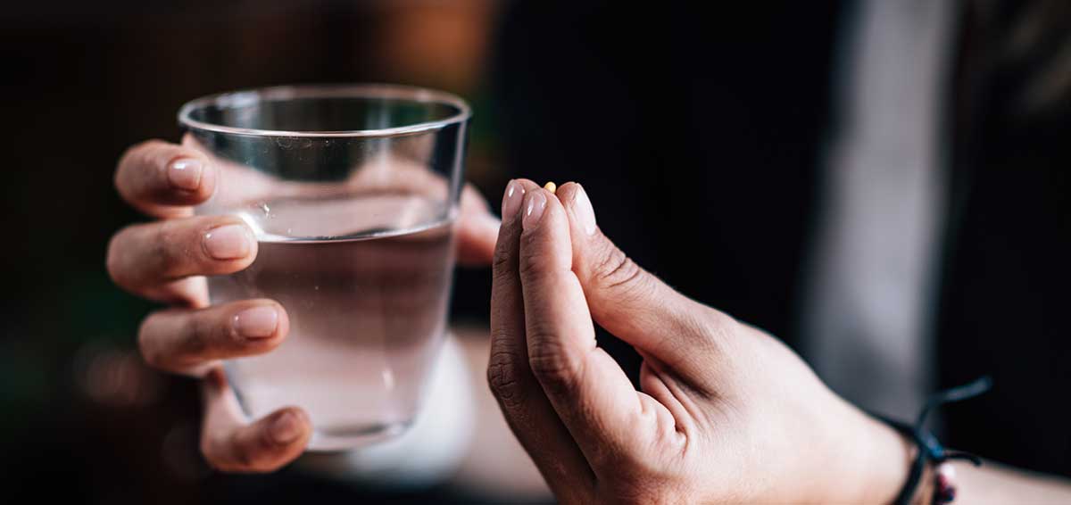 Hände halten Antidepressivum-Pille und ein Glas Wasser